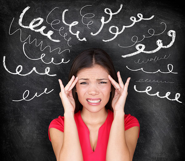 woman with her fingers to her temples distressed in front of a chalkboard with squiggly lines drawn around her head