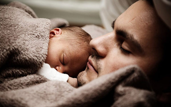 man sleeping in bed with a baby laying on his chest next to his face