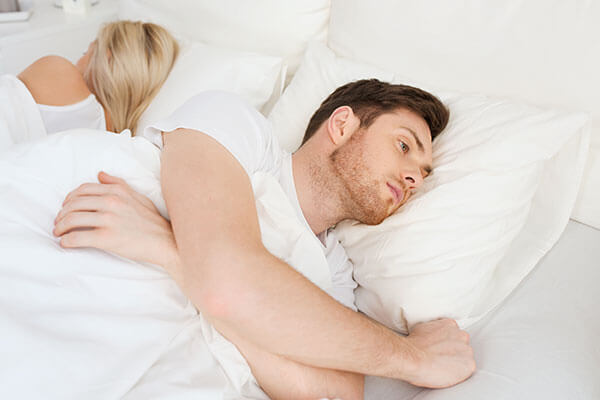 A couple laying in bed with their backs to each other, looking unhappy
