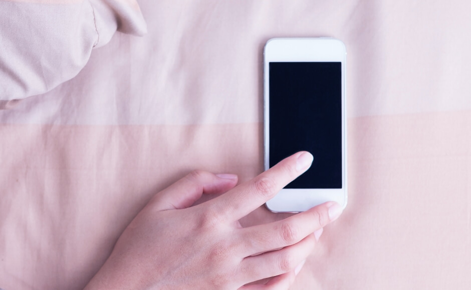 a phone lays on a bed as a woman's hand reaches for it