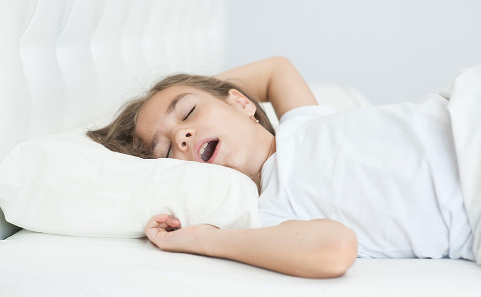 young girl sleeping in a white bed with her mouth open