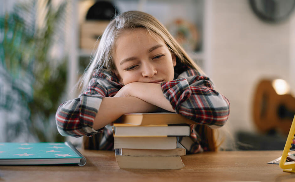 little girl sits at a desk falling asleep on top of a pile of books